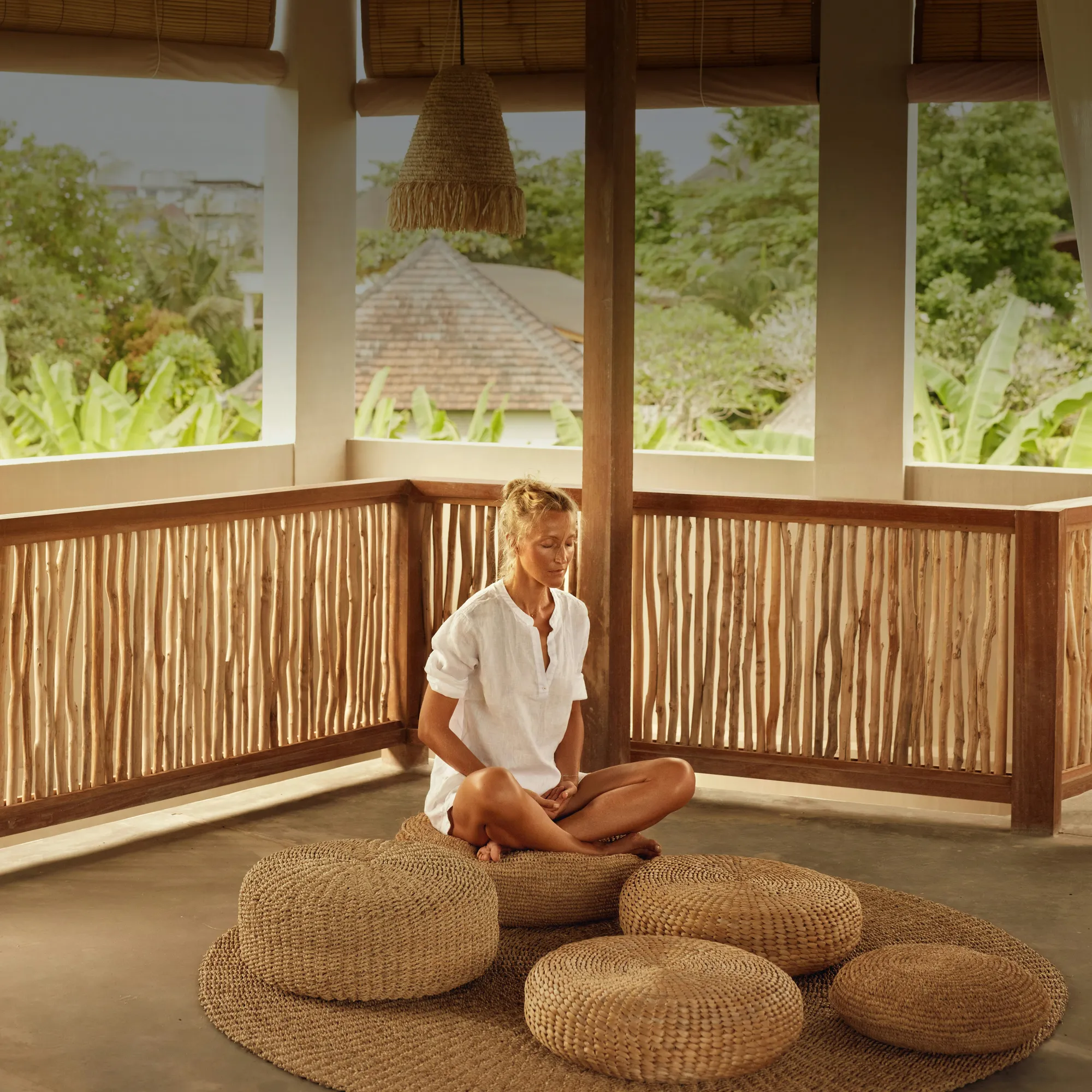 Woman sitting cross-legged in quiet meditation on a sunlit tropical balcony